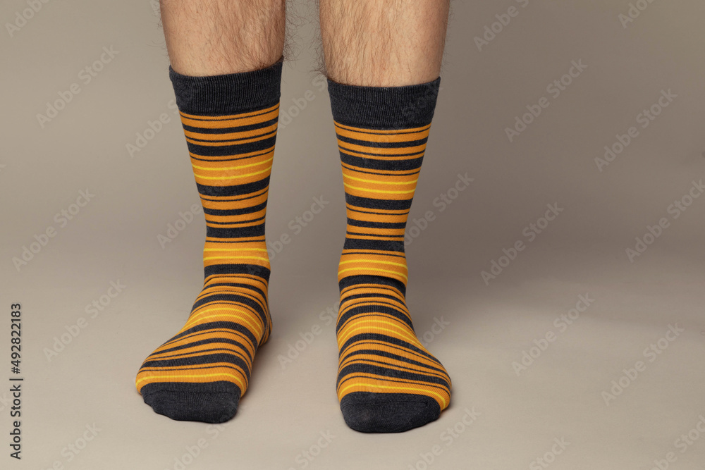 Studio photo of a pair of men's feet wearing yellow and brown striped socks. The background is grey.