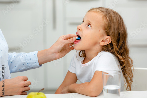 A child with pills, dragees on his tongue. The mother gives the child medicines
