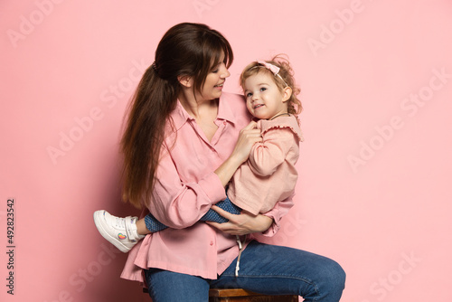 Happy woman and little girl, caring mother and daughter isolated on pink studio background. Mother's Day celebration. Concept of family, childhood, motherhood