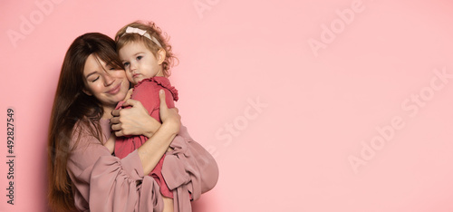 Hugs. Delighted young woman and toddler, caring mother and daughter isolated on pink studio background. Mother's Day celebration. Concept of family, childhood, motherhood