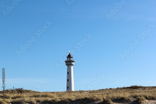 White lighthouse among sandy dunes with blue sky on background.