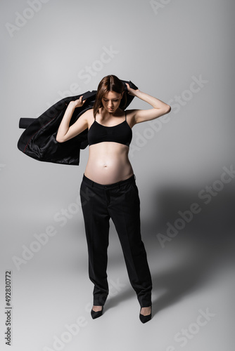 Trendy pregnant woman wearing blazer on grey background