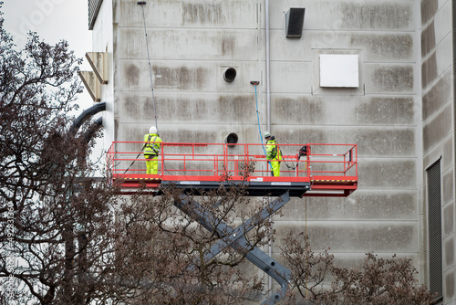 Workers on cherry picker platform using brushes to clean an industrial building