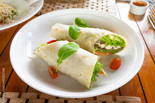 Obraz na płótnie Tortilla wrap with chicken meat and vegetables on traditional dish topping with spinach. w salonie