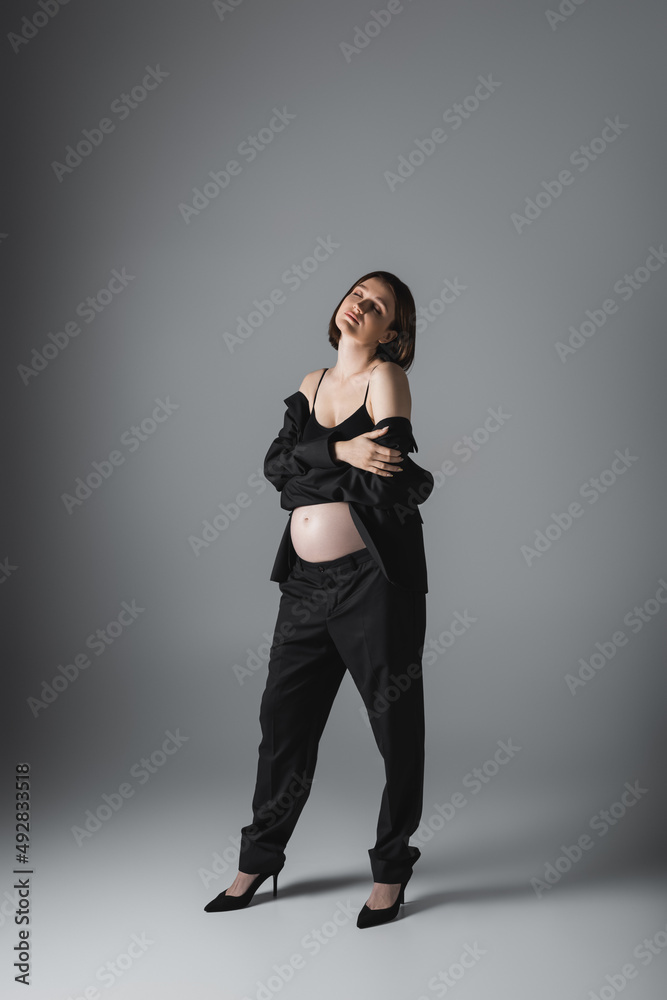 Full length of stylish pregnant woman touching arm on grey background Full length of stylish pregnant woman touching arm on grey background