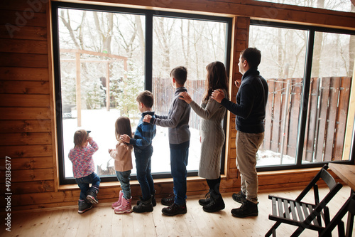 Family with four kids in modern wooden house against large window.
