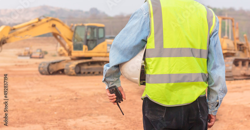 An engineer or worker wearing a life jacket holds a radio transmitter and a white helmet in his hands. for safe working on excavator background