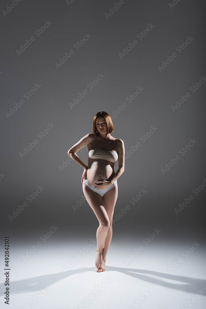 Full length of pregnant woman in panties and top standing on grey background Full length of pregnant woman in panties and top standing on grey background
