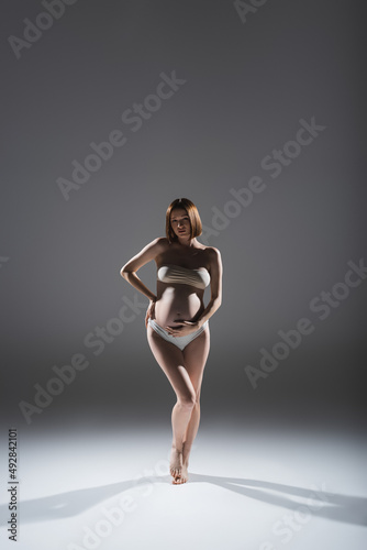 Full length of pregnant woman in panties and top standing on grey background