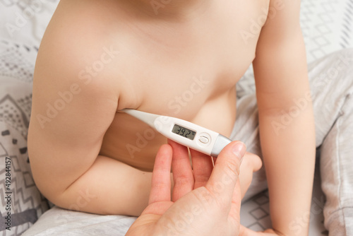 A mother or nurse measures the temperature of a 4-year-old boy with an electronic thermometer