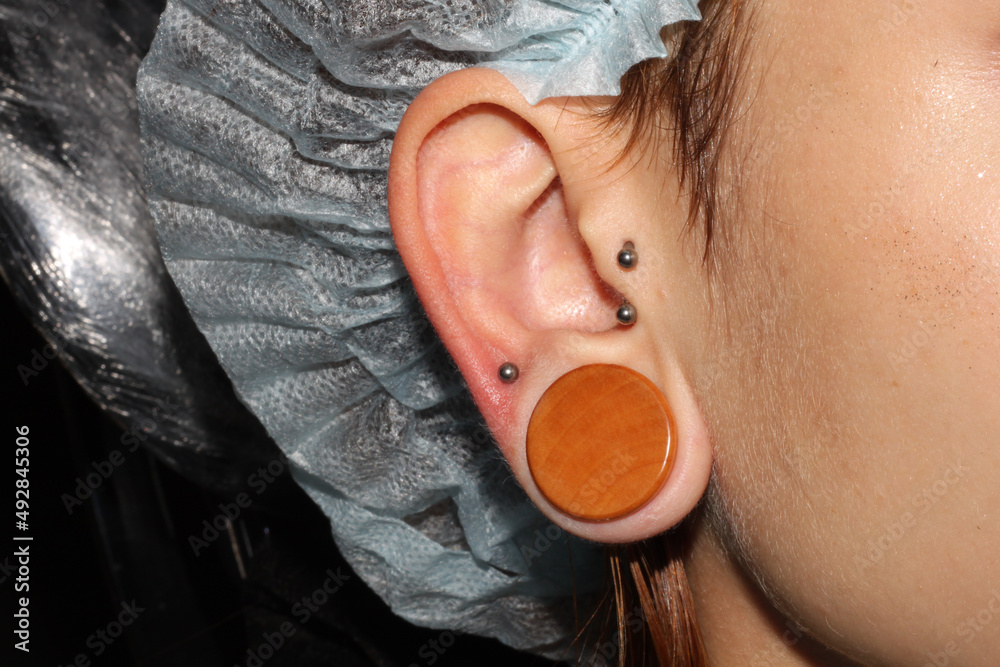 Girl ear piercing. Wood tunnel. Tragus piercing + circular with balls. Ear  lobe piercing with titanium labret. Photos | Adobe Stock