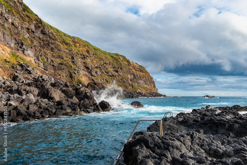 Selective focus on metal stairs in volcanic rocks for oceanic and geothermal pool with wave breaking on rocks in Ponta da Ferraria, São Miguel - Azores PORTUGAL