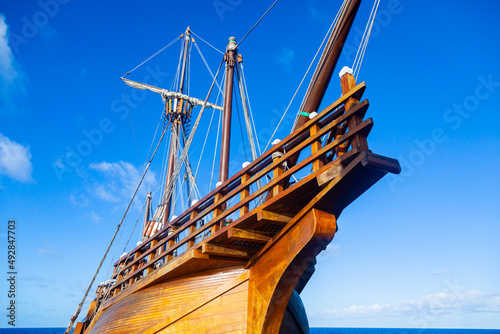 An old wooden caravel ship with folded sails against a blue sky with white clouds. photo
