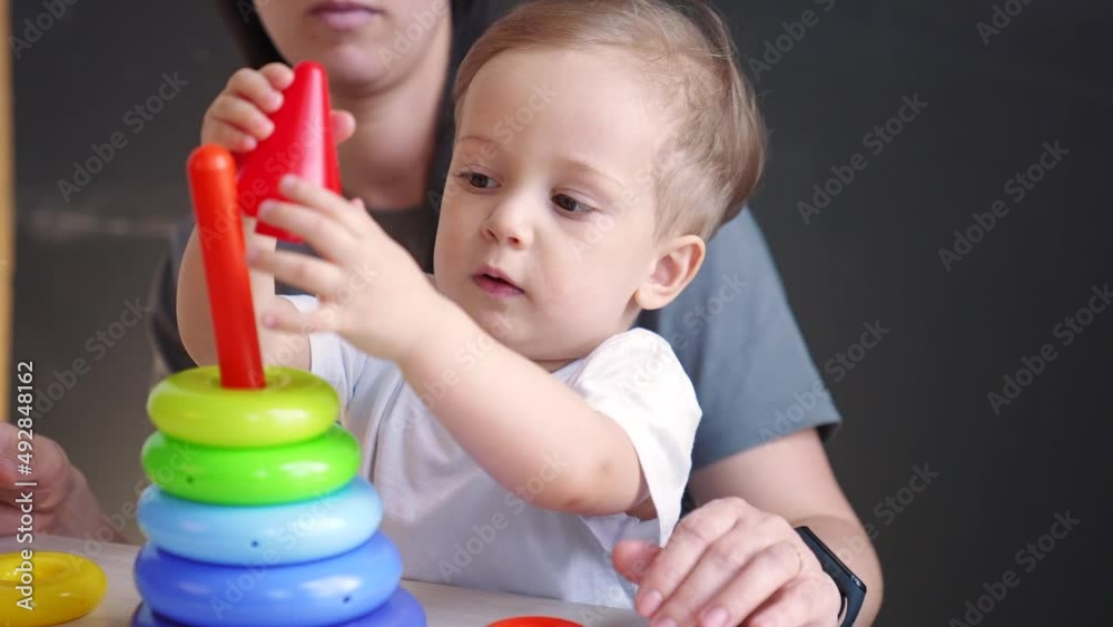 baby collects toy pyramid. mom plays with her son at home happy family. development of fine motor skills in newborn child. happy family mom and baby play preschool pyramid toy. kindergarten education baby collects toy pyramid. mom plays with her son at home happy family. development of fine motor skills in newborn child. happy family mom and baby play preschool pyramid toy. kindergarten education