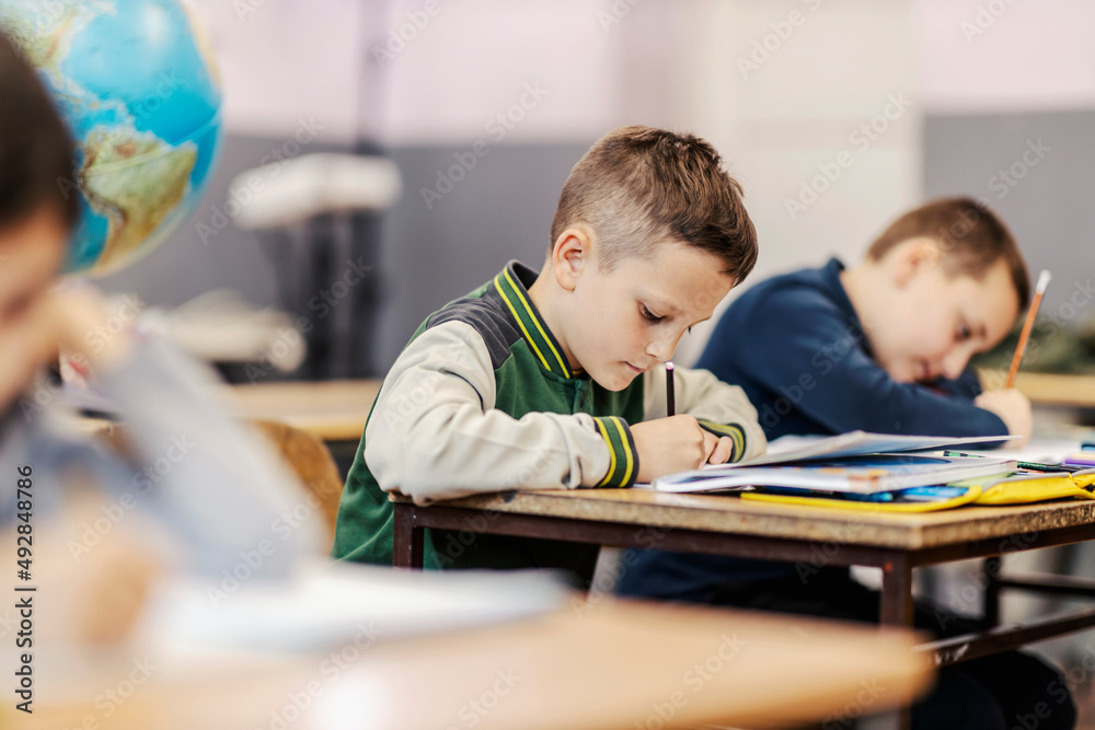 Fototapeta premium A schoolboy writing down schoolwork at classroom.