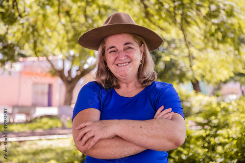 Happy female farmer smiling at camera with arms crossed. Portrait of smiling beautiful female farmer. Woman at farm in summer day. Gardening activity. Brazilian elderly woman. Latino people.