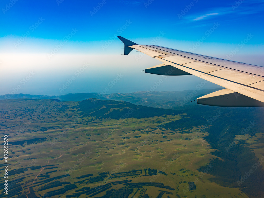 Obraz premium View of airplane wing, blue skies and green land during landing. Airplane window view.
