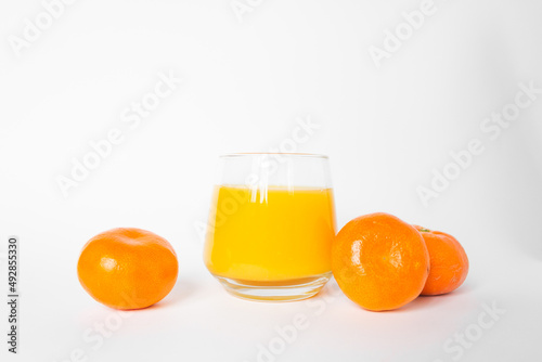 Glass of fresh orange juice with three citrus mandarin fruits near. Isolated on the white background.