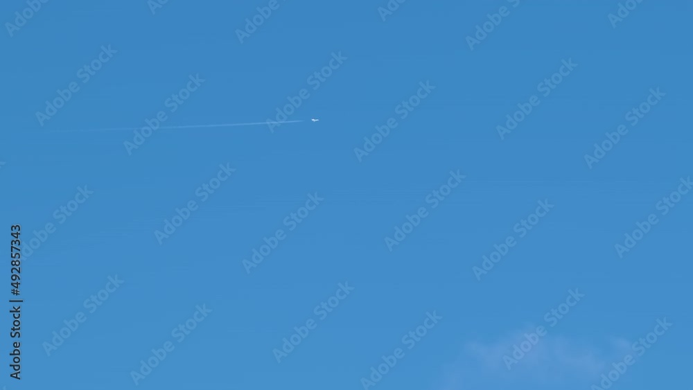 Distant passenger jet plane flying on high altitude on clear blue sky leaving white smoke trace of contrail behind. Air transportation concept Distant passenger jet plane flying on high altitude on clear blue sky leaving white smoke trace of contrail behind. Air transportation concept