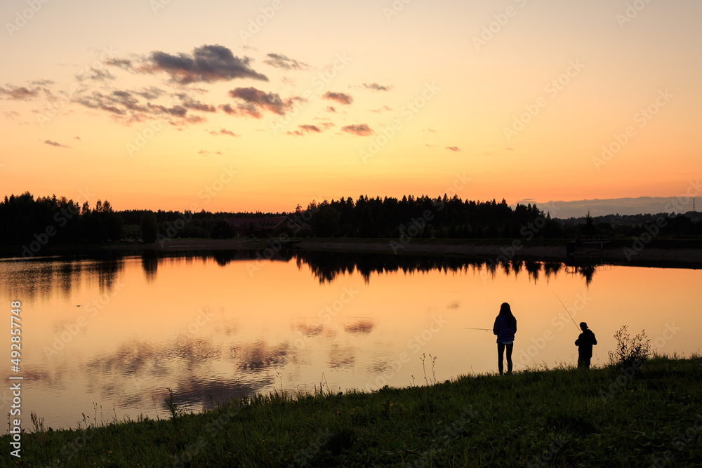 Sunset on the lake and silhouettes of people, against the background of the forest, summer, orange sky.