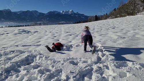 A couple jumping on an alpine meadow covered with fresh powder snow near Kathreinkogel in Schiefling am See in Carinthia, Austria. Scenic view on the mountain peaks of the Karawanks. Winter activity
 photo