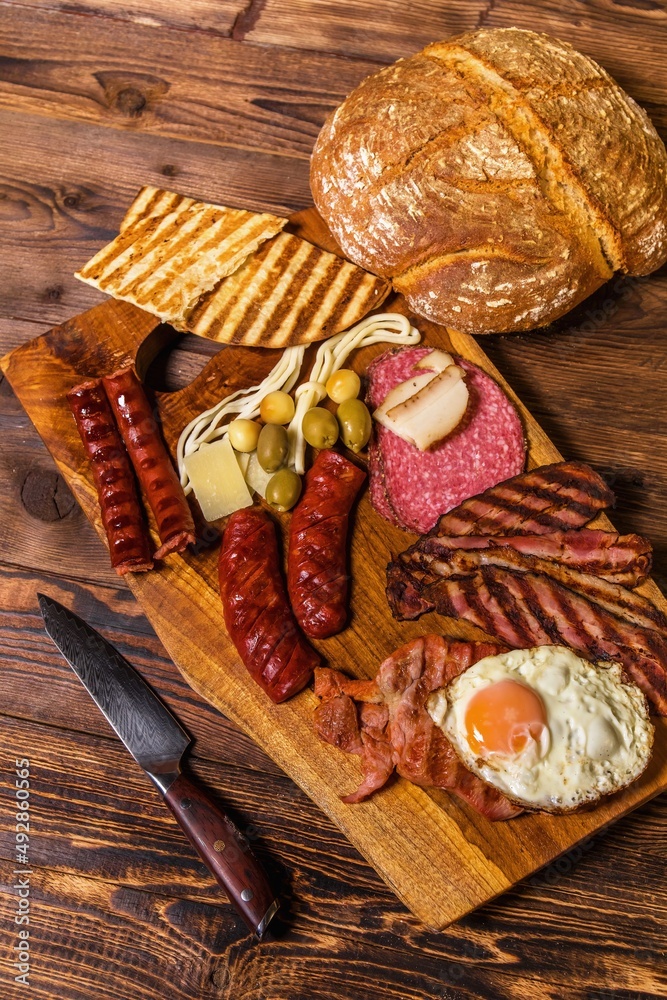 Different kinds of grilled sausages with egg. A selection of grilled gourmet meats on a rustic timber board. Grilled sausages with homemade bread.