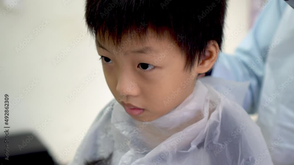 Kid and barber wear gown during hair cutting as SOP stated in barbershop during coronavirus pandemic. Kid and barber wear gown during hair cutting as SOP stated in barbershop during coronavirus pandemic.