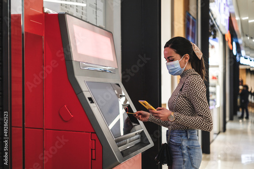 a young woman with mask getting money from an atm machine