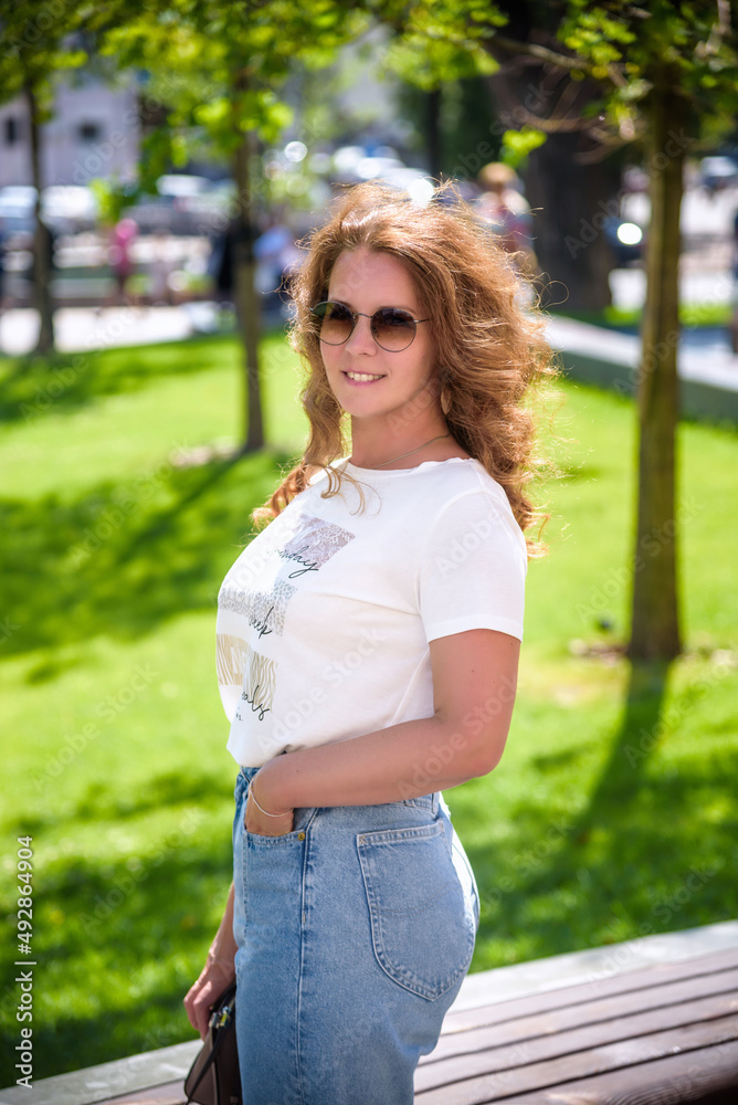 Close-up portrait of laughing brunette girl in casual clothes, sunglasses and jeans on city background. Lovable lady standing on city street and looking directly on camera Close-up portrait of laughing brunette girl in casual clothes, sunglasses and jeans on city background. Lovable lady standing on city street and looking directly on camera