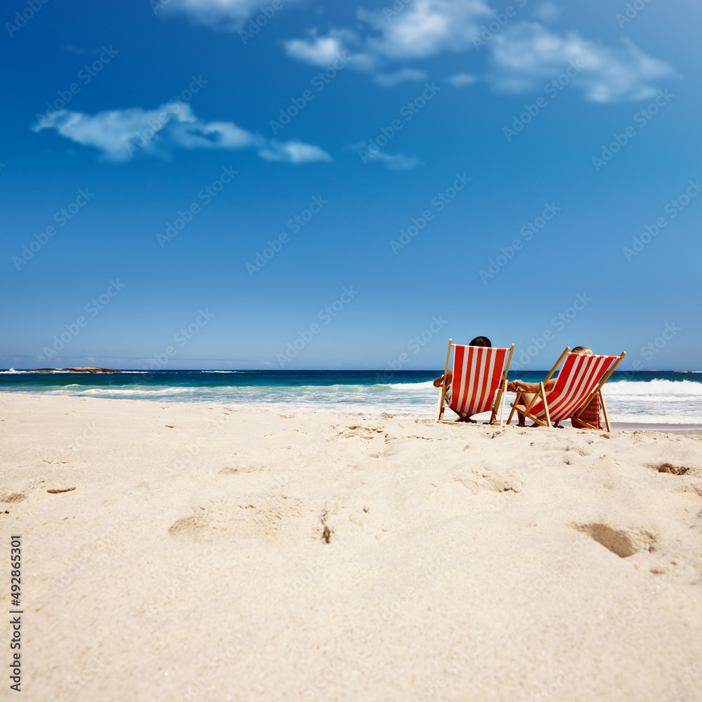 Getting away from it all. Rearview shot of an affectionate couple reclining on their deck chairs at the waters edge. Getting away from it all. Rearview shot of an affectionate couple reclining on their deck chairs at the waters edge.