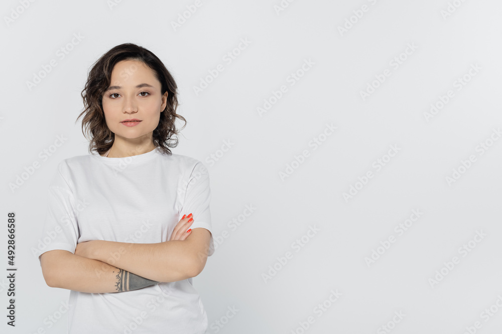 Tattooed brunette woman crossing arms isolated on grey. Tattooed brunette woman crossing arms isolated on grey.