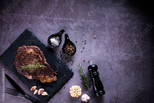 Sliced beef ribeye steak, grilled with 4seasons pepper garlic-rosemary, on stone plate dark and dark grey background, knife and fork black, top view photo