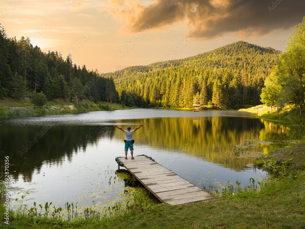 Beautiful lake in the forest at sunset. Man on wooden pier with open arms.
