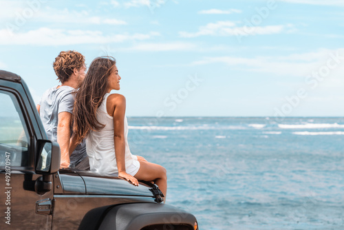 Car road trip travel couple tourists enjoying ocean view relaxing on hood of sports utility car. Happy Asian woman, man friends smiling on beach. photo
