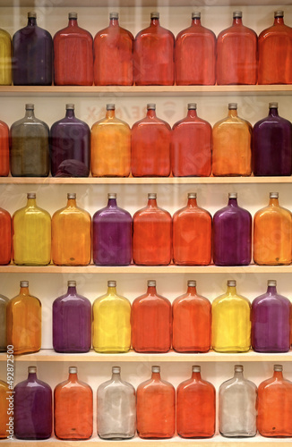 many colored glass bottles red orange violett in 3 lines on a shelf 