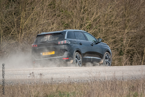Black Peugeot 5008 GT sport utility vehicle driving along an unmade stone track road thowing up dust