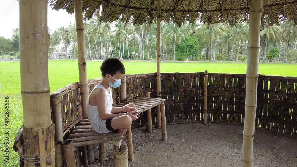 Asian kid wear face mask with bare foot hide in the wooden house play hand phone Asian kid wear face mask with bare foot hide in the wooden house play hand phone