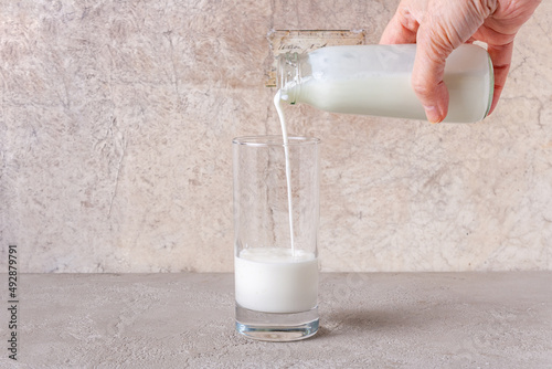 yogurt is poured from a bottle into a glass on a beige background, copy space