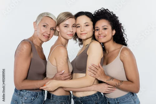 Obraz Multiethnic women hugging and smiling at camera isolated on grey, feminism concept.