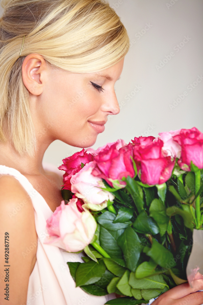 Stopping to smell the roses. Cropped shot of a young woman holding a bouquet of pink roses in profile.