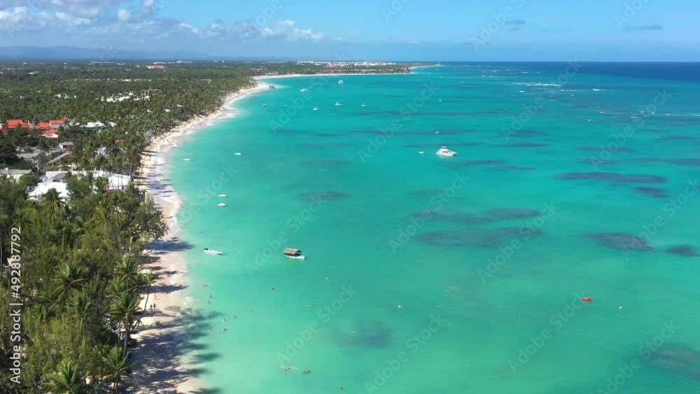 Tropical coastline with resorts, palm trees and caribbean sea with floating boats and people having fun doing paraseiling. Travel destinations. Dominican Republic. Aerial view Tropical coastline with resorts, palm trees and caribbean sea with floating boats and people having fun doing paraseiling. Travel destinations. Dominican Republic. Aerial view