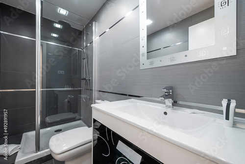 Toilet with white wooden furniture with drawers  mirror with frame and stainless steel and glass screen with white porcelain toilets