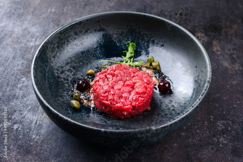 Modern style gourmet tartar raw from beef filet with capers and amarena cherry served with truffle cream and lettuce as close-up in a Nordic design plate photo