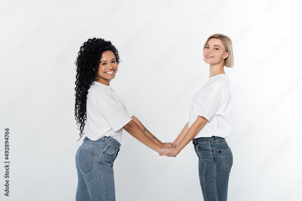 Young interracial women holding hands isolated on grey. Young interracial women holding hands isolated on grey.