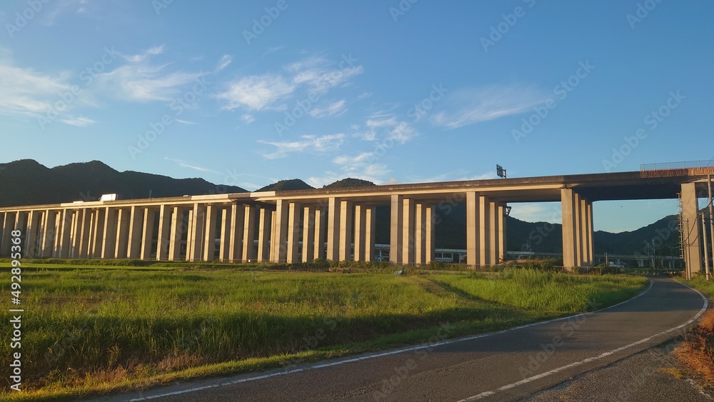 田畑の中にある夕日に照らされる高架高速道路と青空その奥には新幹線