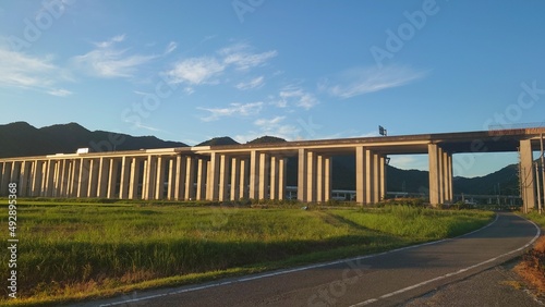 田畑の中にある夕日に照らされる高架高速道路と青空その奥には新幹線 © 雑猫