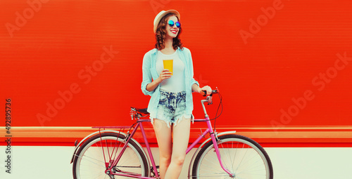 Summer colorful image of happy smiling young woman with bicycle on vivid red background