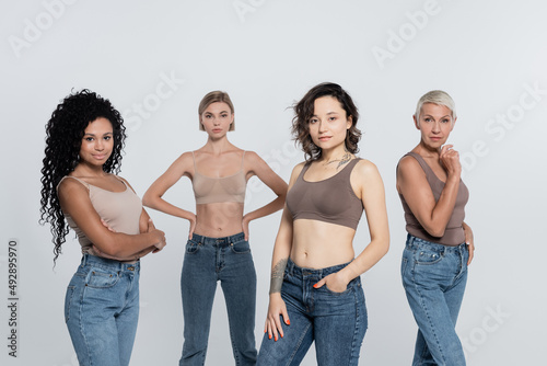 Brunette woman in top posing near interracial friends isolated on grey, feminism concept. © LIGHTFIELD STUDIOS