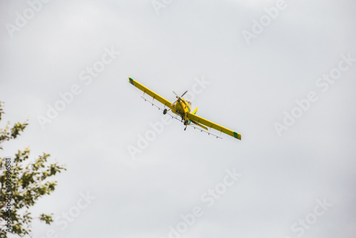 The underside of a yellow crop dusting sptay plane flying in the air