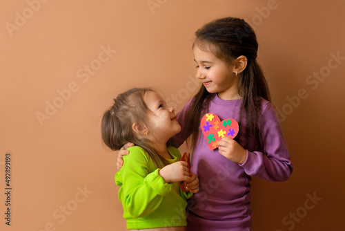 Girls look at each other, holding handmade cards with puzzles in their hand. The eldest child teaches his sister support, care and love by his own example. Symbol of autism day. No discrimination photo